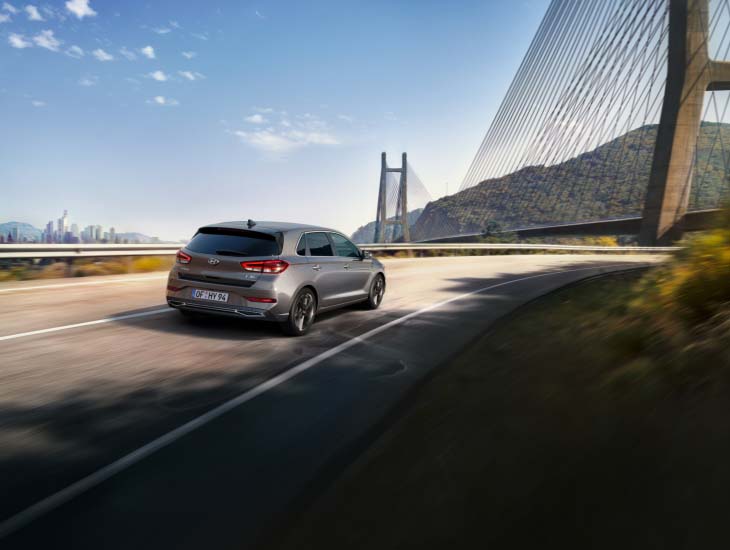 Woman with a smartphone holding in her hand, the new Hyundai i30 in the background.